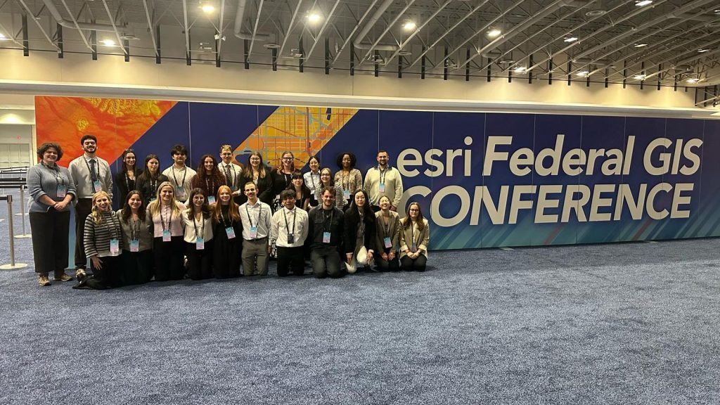 A group photograph of conference-goers in front of an esri Federal GIS Conference banner.